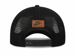 Back view of a black Nike mesh trucker cap with an adjustable snap strap and brown leather logo patch on the back panel.