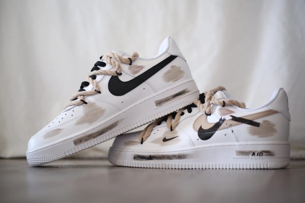 White Nike sneakers with beige paint splashes and a black swoosh on a light background.