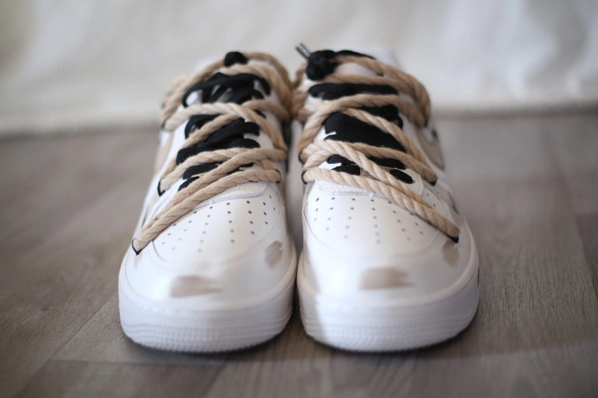 Close-up of white sneakers with beige laces tied in loops on a wooden floor, viewed from the front.