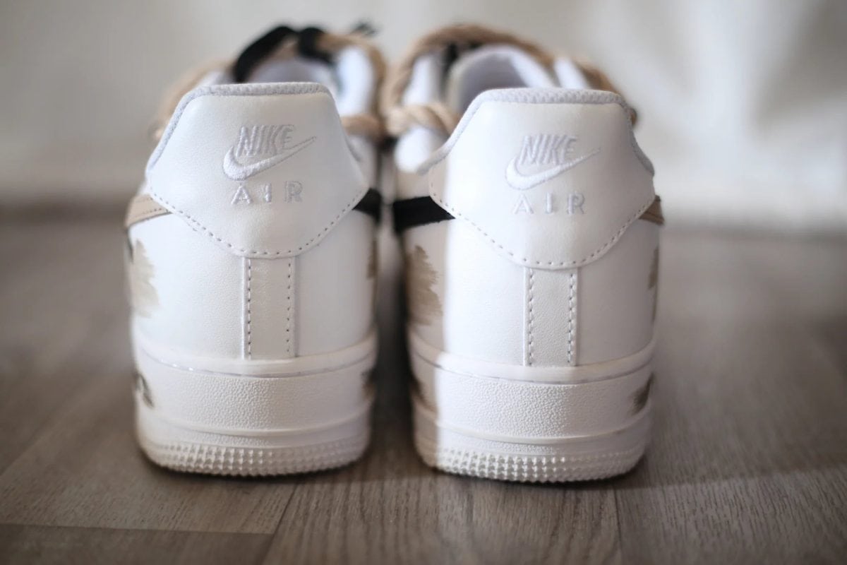 Rear view of white Nike Air sneakers with embossed Nike swoosh and Air branding, on a wooden floor.