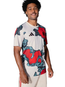 Man wearing a bold white, red, and teal camo-patterned Adidas athletic jersey with the Adidas logo on the chest, standing and smiling outdoors.