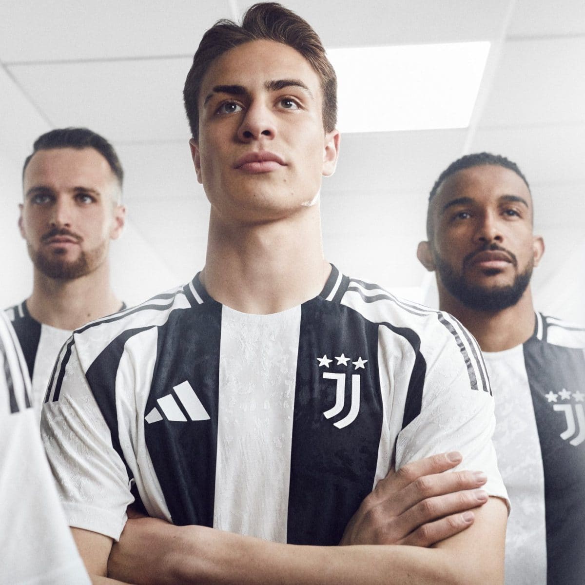 Three soccer players wearing Juventus black-and-white striped jerseys stand with crossed arms in a bright room, posing for a team photo.