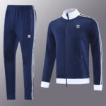 Navy blue Adidas tracksuit jacket with white stripes and zipped pockets, paired with matching navy pants featuring white side stripes.