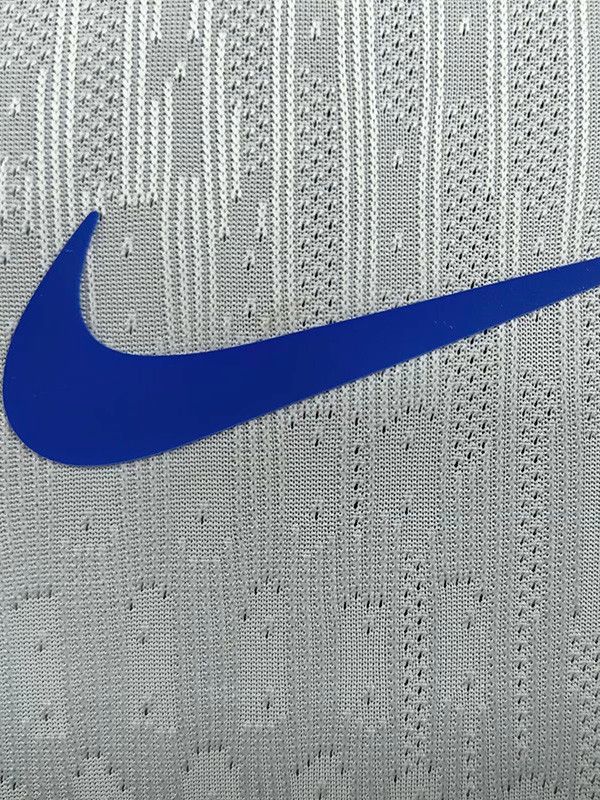 9a32c5f0-e2ce-44b1-9714-492040a376ea | UAE SPORT STORE Close-up of a blue Nike swoosh on light gray knitted fabric, likely a garment surface.