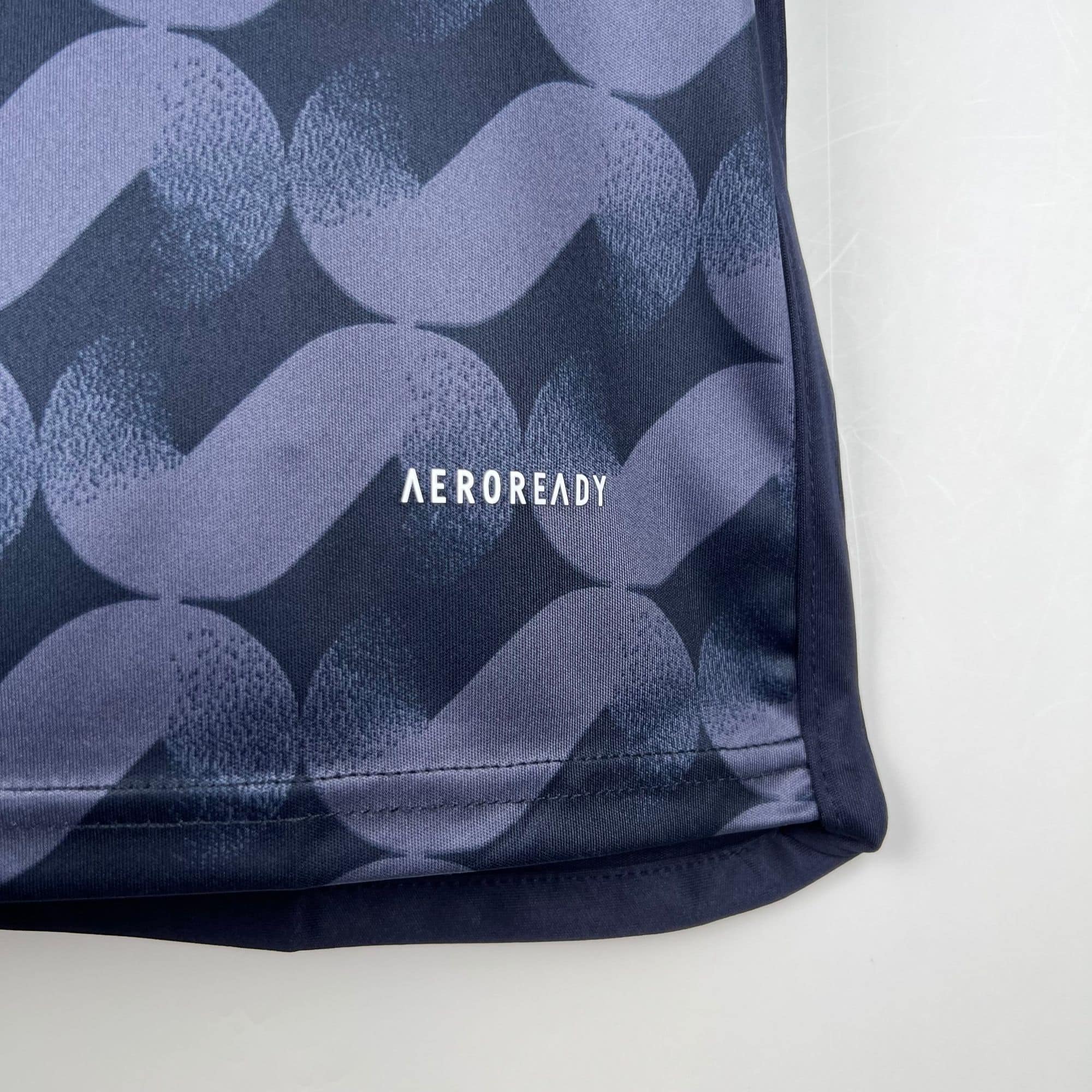 9a7d002d | UAE SPORT STORE Close-up of dark blue fabric with a repeating light-blue circular pattern and the partial word 'AEROREADY'.