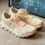 9aabd2be-1e26-4b11-93e2-4402d0527344 | UAE SPORT STORE Beige knit running shoes with a thick white sole and laces, pair resting on a concrete floor.