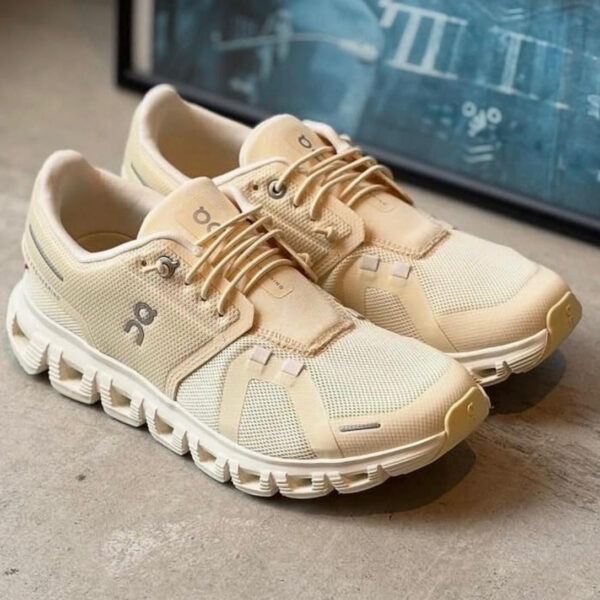 Beige knit running shoes with a thick white sole and laces, pair resting on a concrete floor.