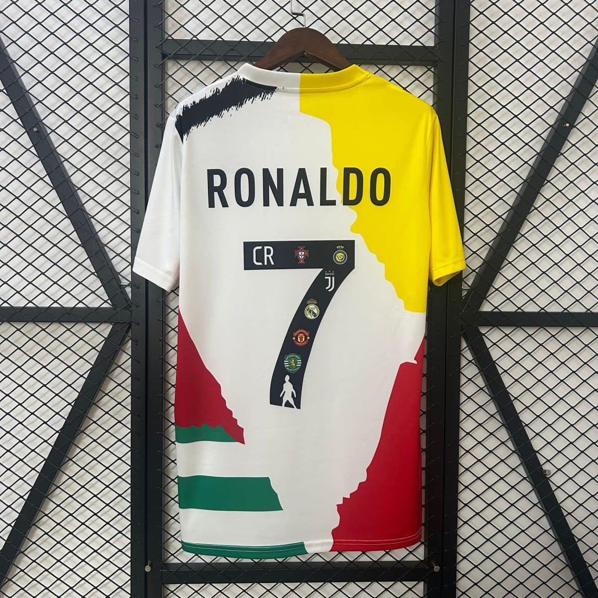 Back view of a Portugal-themed soccer jersey with 'RONALDO' printed across the back, featuring white and yellow color blocks and green-red trim, on a hanger against a wire grid backdrop.