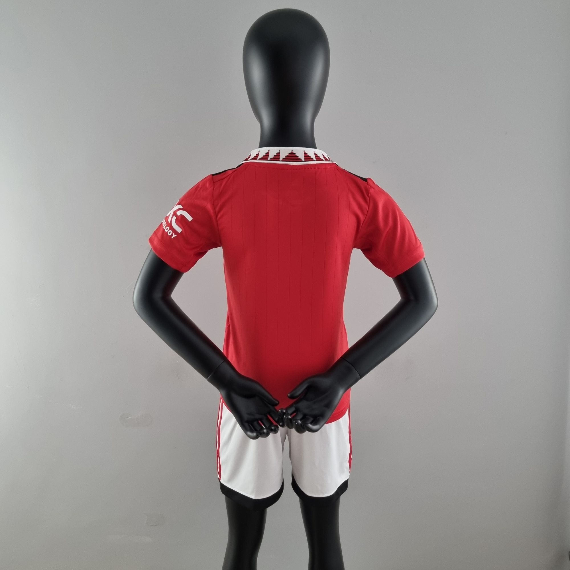 9b4a20c1_74528992-6b1b-491b-bec7-034703a7f048 | UAE SPORT STORE Back view of a black mannequin wearing a red athletic jersey with a white patterned collar and white shorts with red trim, arms crossed behind the back.