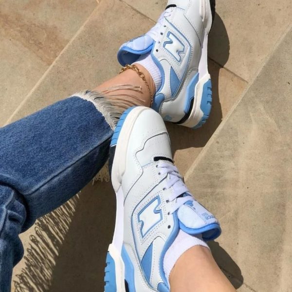 White and sky-blue sneakers with chunky soles worn with ripped jeans, shown from above on a tan tiled surface.
