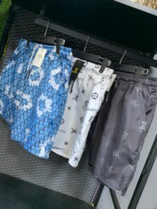 Blue patterned shorts with repeating logo on a rack, tag visible, alongside white and gray designer shorts in a store display
