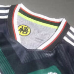 9baeb6d147322f5d | UAE SPORT STORE Close-up of a dark athletic jersey collar with white, red, and black trim; Adidas label on mesh inside and a yellow circular symbol with a character.