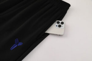 Black athletic pants with a blue embroidered logo, a smartphone tucked into the pocket.