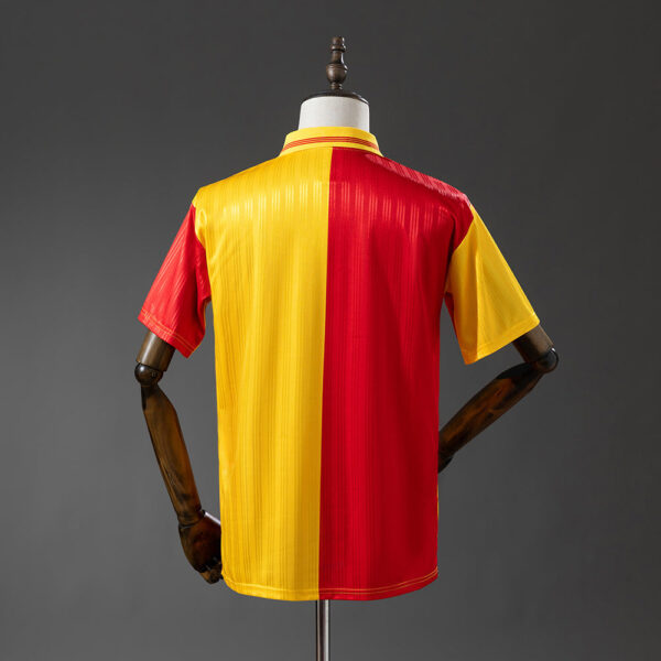 Back view of a color-block jersey: yellow panel on the left, red panel in the center, and a yellow sleeve on the right, displayed on a mannequin against a gray backdrop.