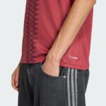 9d0c7e53-cac6-43bf-81ad-7cb7ea7effc2 | UAE SPORT STORE Side view of a person wearing a red athletic shirt with a zigzag stripe and a small ClimaCool logo, paired with dark jeans with white vertical stripes near the pocket.