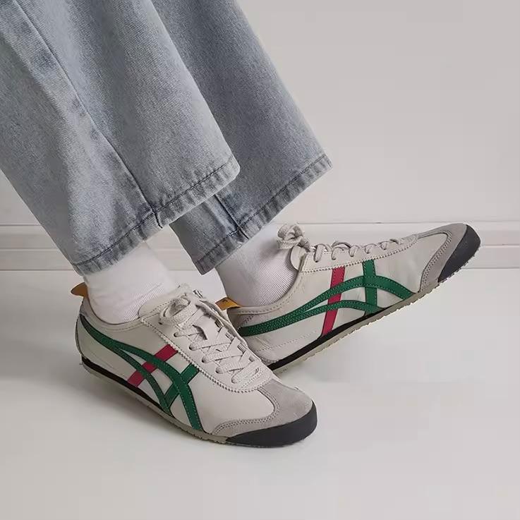 9d4c2d5b-ea99-4c4d-bbfb-bb4d91f692b1 Person wearing white sneakers with green and pink stripes, standing on a white floor with light-wash jeans cuffed at the ankle