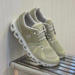 Pair of light beige On running shoes with white soles resting on a metal rack.