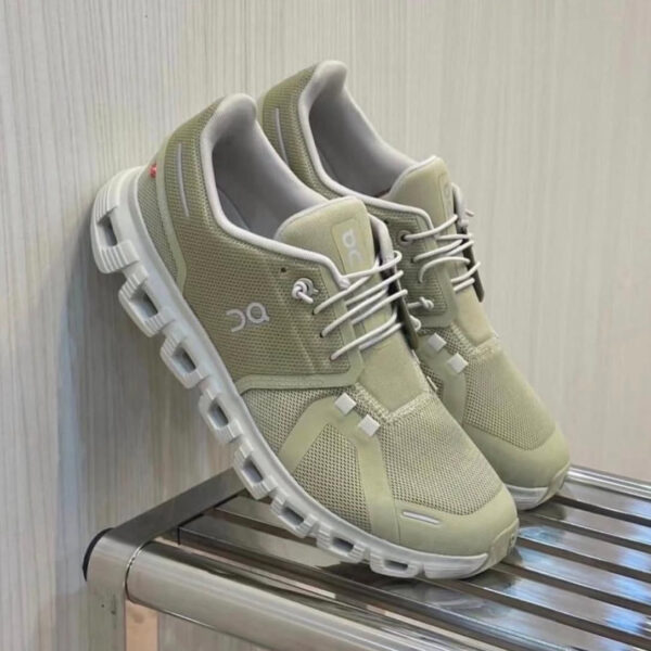 Pair of light beige On running shoes with white soles resting on a metal rack.