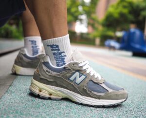 Close-up of gray New Balance 2002R sneakers on a runner's feet with white socks on a green track surface.