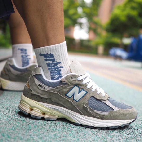 Close-up of gray New Balance 2002R sneakers on a runner's feet with white socks on a green track surface.
