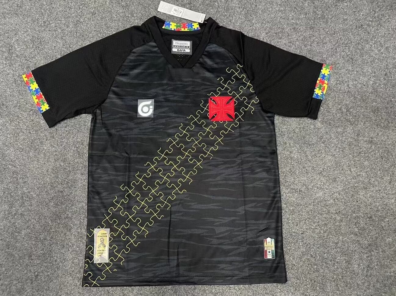 9d815e3b | UAE SPORT STORE Black athletic jersey with yellow puzzle-piece diagonal pattern and colorful sleeve trim; features red crest patch and small patches near hem.
