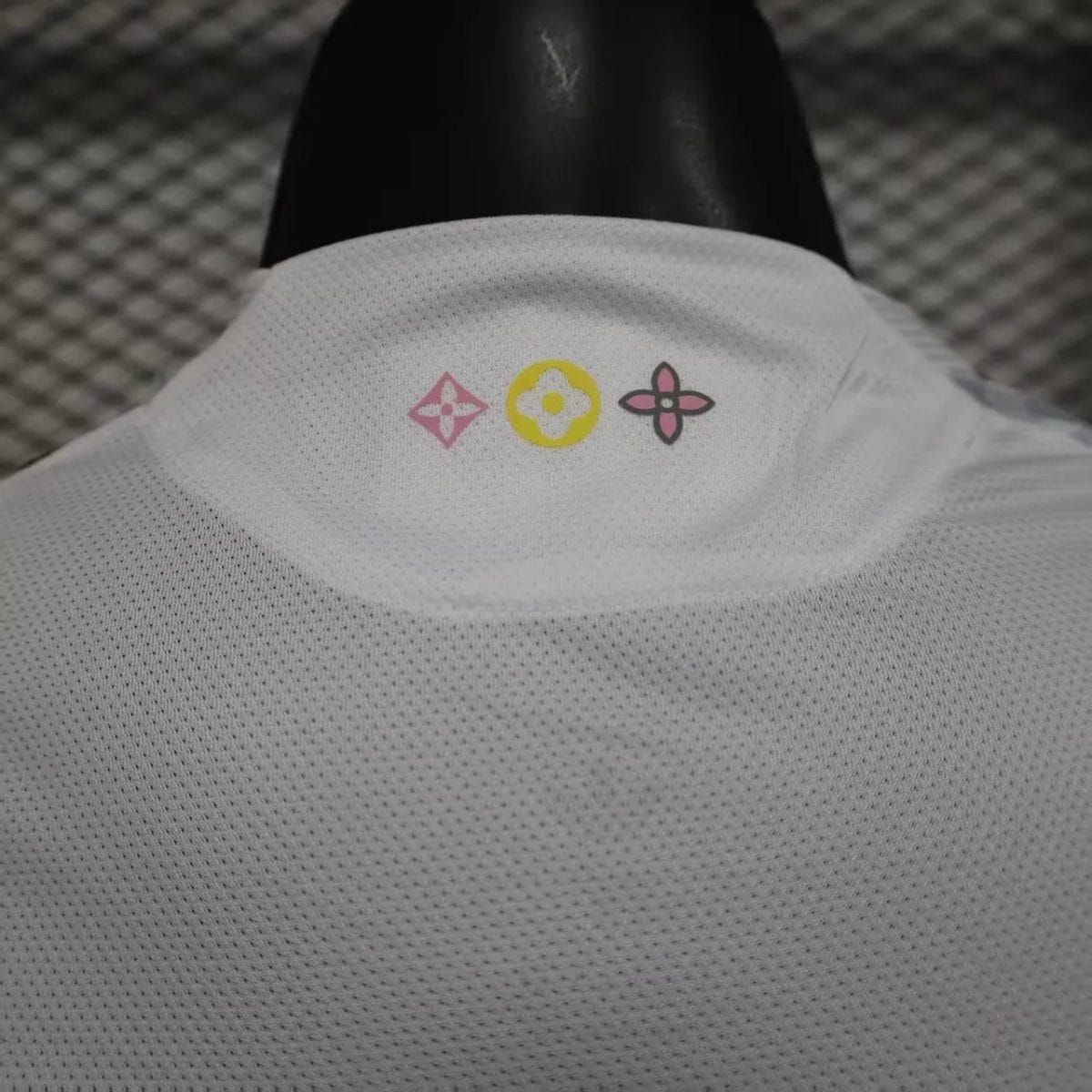White mesh collar with three small decorative logos in pink, yellow, and pink placed along the back edge of the garment
