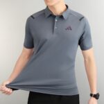 Person wearing a gray polo shirt with a small three-triangle logo on the left chest, pulling the hem downward.