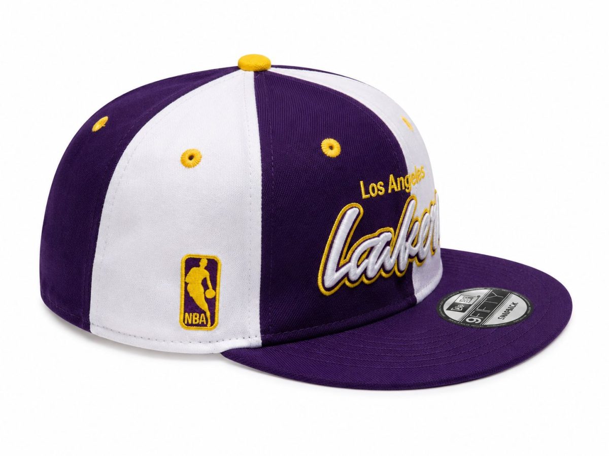 Purple and white Lakers snapback cap with yellow embroidered lettering and NBA logo patch on the side.