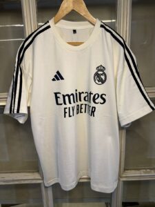 White Real Madrid football jersey on a hanger, size XL, featuring the Emirates Fly Better sponsor and Adidas stripes on the sleeves.