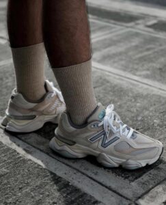 Beige New Balance sneakers with white laces on a gray concrete pavement, worn with light-brown socks.