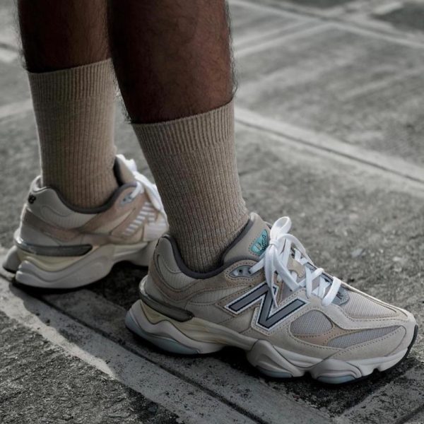 Beige New Balance sneakers with white laces on a gray concrete pavement, worn with light-brown socks.