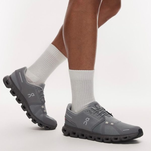 Gray athletic shoes with a chunky segmented sole, worn with white crew socks during a mid-step pose.
