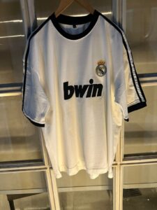 White Real Madrid football jersey on a hanger, featuring the Real Madrid crest and 'bwin' sponsor logo.