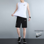 Male model wearing a white Nike Pro sleeveless shirt and black Nike shorts, pulling at his shirt.