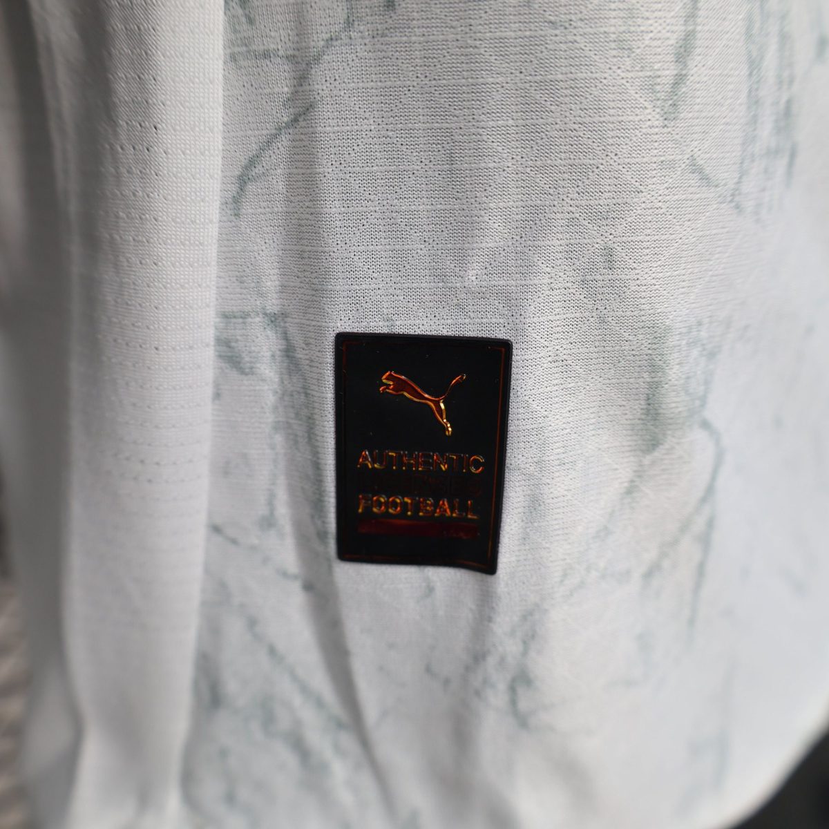 Close-up of gray textured fabric with a small black badge displaying a gold leaping animal logo and text.