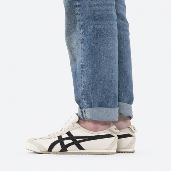 Person wearing light-wash rolled-hem jeans and cream sneakers with black side stripes, standing sideways in profile view