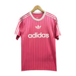 Pink Adidas T-shirt on a hanger with white stripes on shoulders and the Adidas logo and text across the chest.