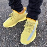 Yellow knit sneakers with pale laces on a person standing on asphalt in dark jeans (close-up).