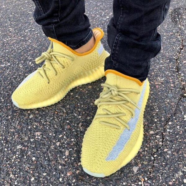 Yellow knit sneakers with pale laces on a person standing on asphalt in dark jeans (close-up).