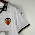 Close-up of a white Valencia CF soccer jersey with the club crest on the chest and black-gold striped collar detail.