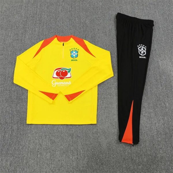 Yellow Brazil goalkeeper jersey with red accents and matching black pants laid flat on gray carpet, sponsor logo on front.