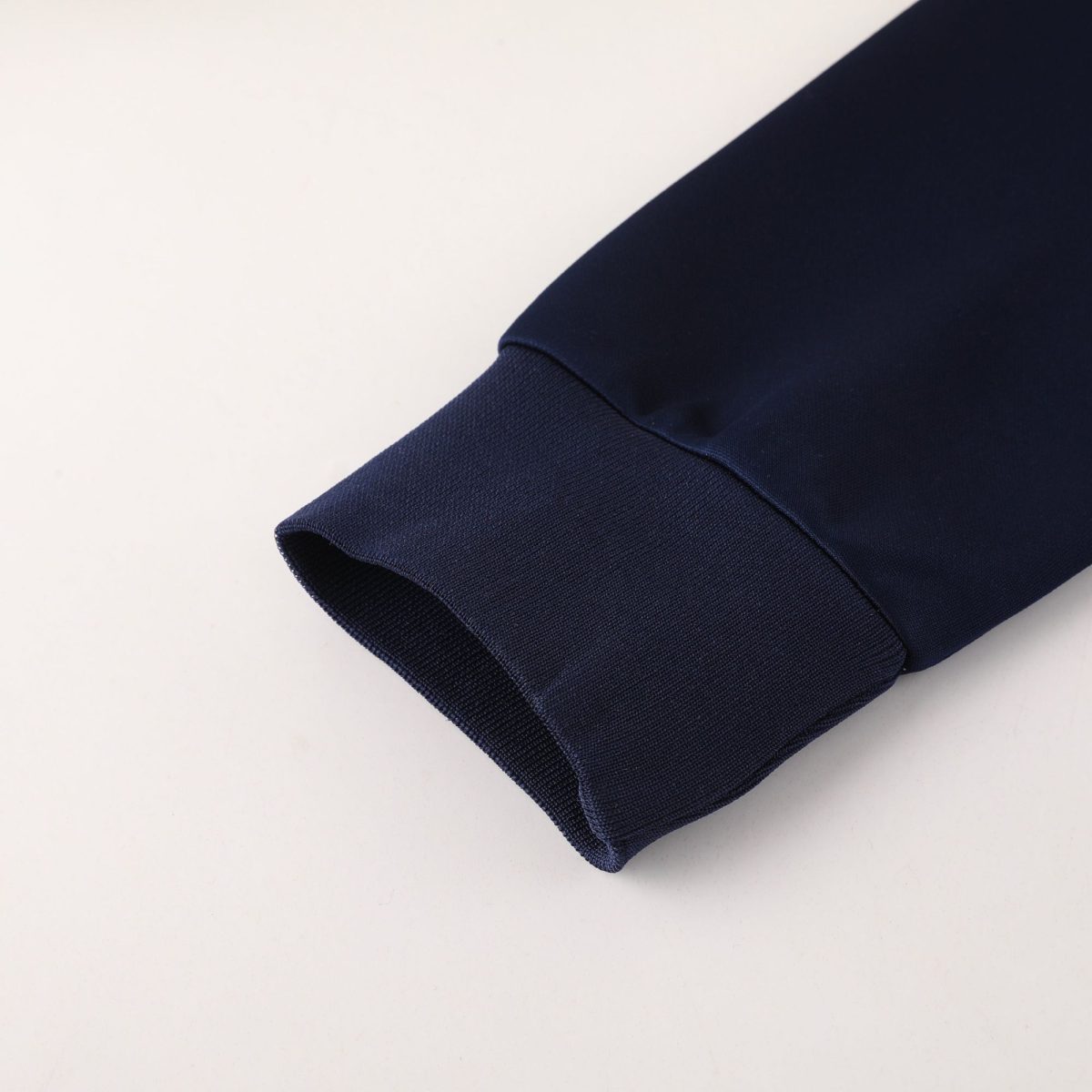 Close-up of navy blue fabric cuff with textured knit and visible seam against a light background, diagonal placement.