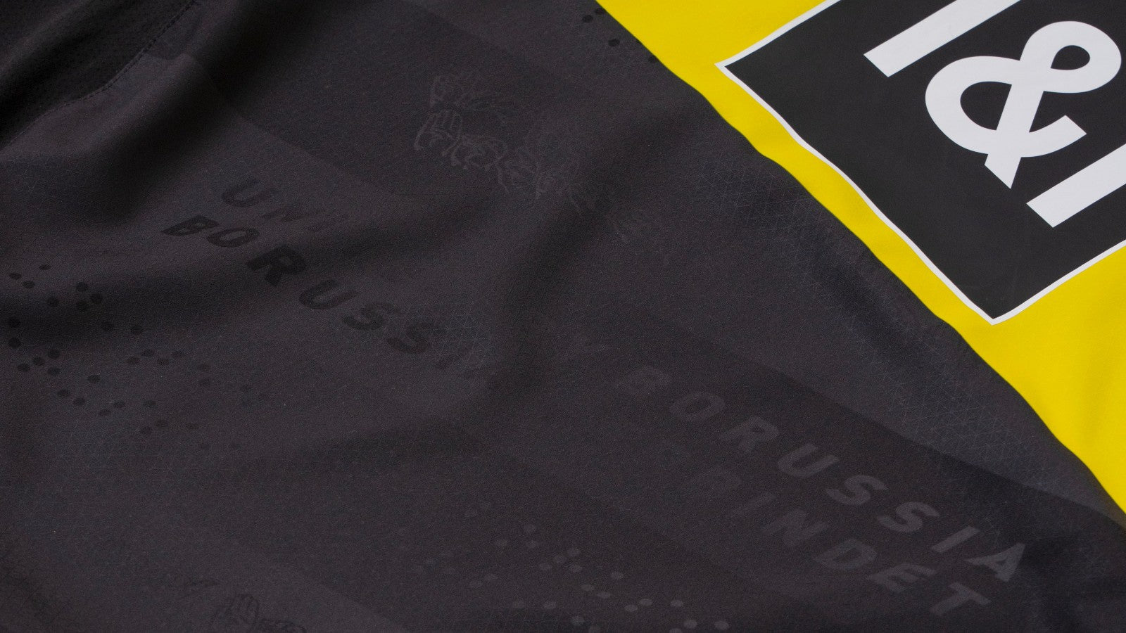 9n60UtW8sHjMlkX | UAE SPORT STORE Close-up of dark fabric with a bright yellow border and partial white logo, suggesting a product branding context.