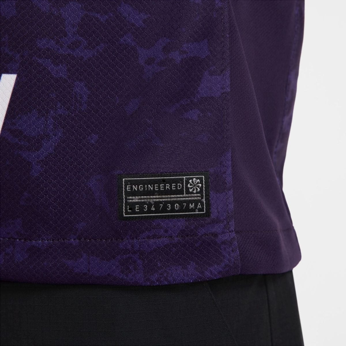 Close-up of a purple jacket fabric with a black ENGINEERED patch and numeric code near the hem.