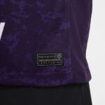 Close-up of a purple jacket fabric with a black ENGINEERED patch and numeric code near the hem.