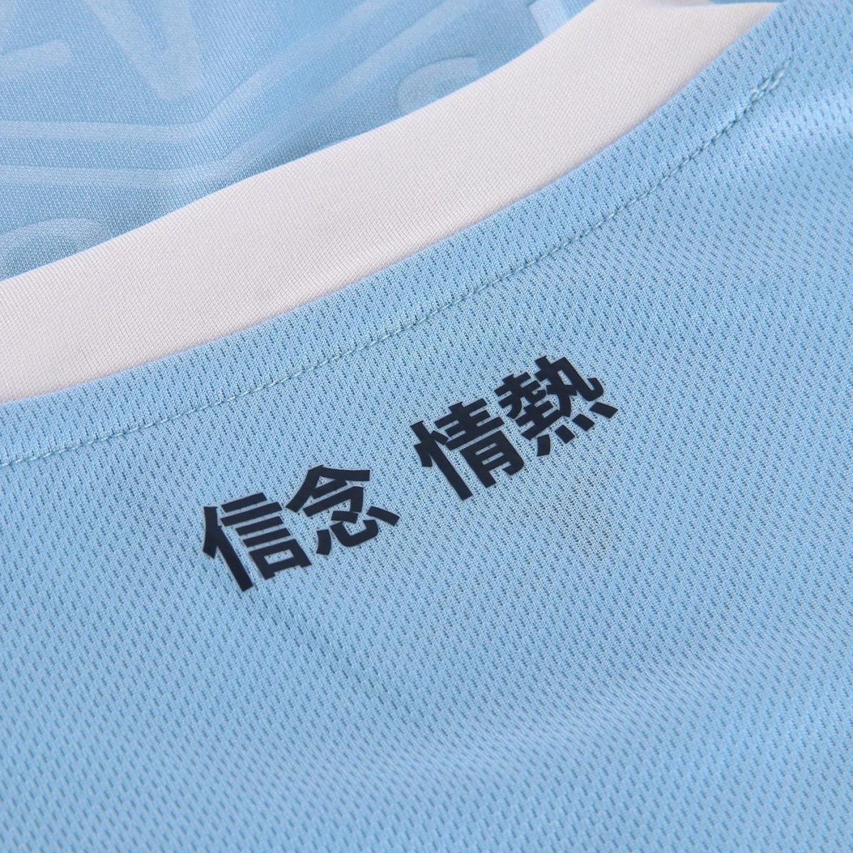 Close-up of light blue fabric with a white collar and black Japanese characters reading 信念 and 情熱 along the seam, conveying belief and passion.