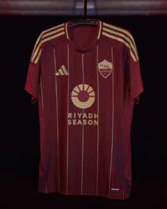 Maroon AS Roma soccer jersey on hanger featuring gold sponsor logo 'RIYADH SEASON' and crest, striped sleeves.
