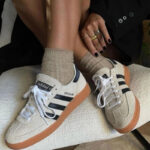 Beige Adidas Spezial sneakers with white laces and black stripes resting on a light cushion, beige socks visible.