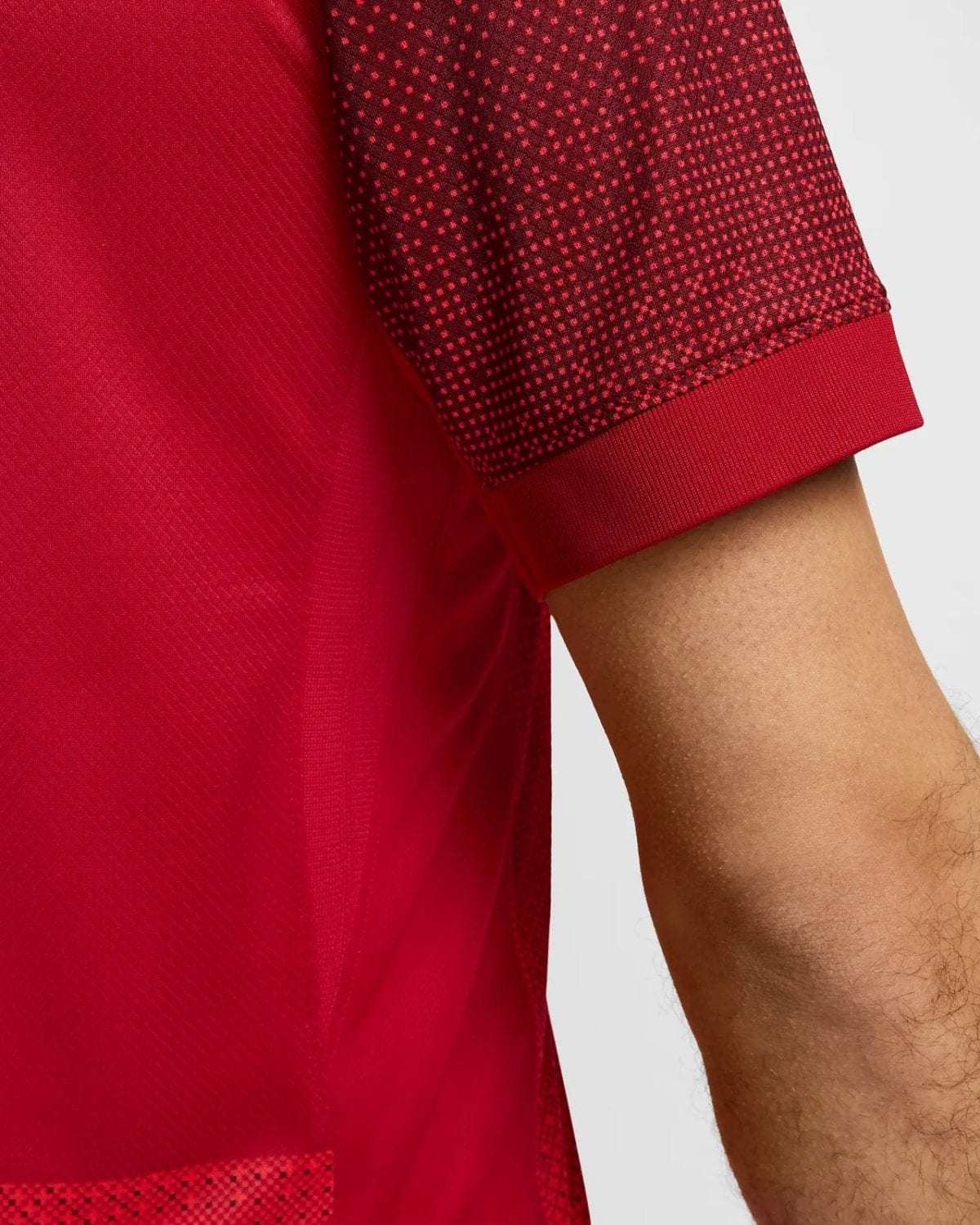 Close-up of a red short-sleeve jersey sleeve with a dark red-to-black dotted pattern at the cuff edge and a solid red body behind it.