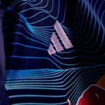 Close-up of a blue sports jersey with a white Adidas logo and wavy line pattern in the fabric design.